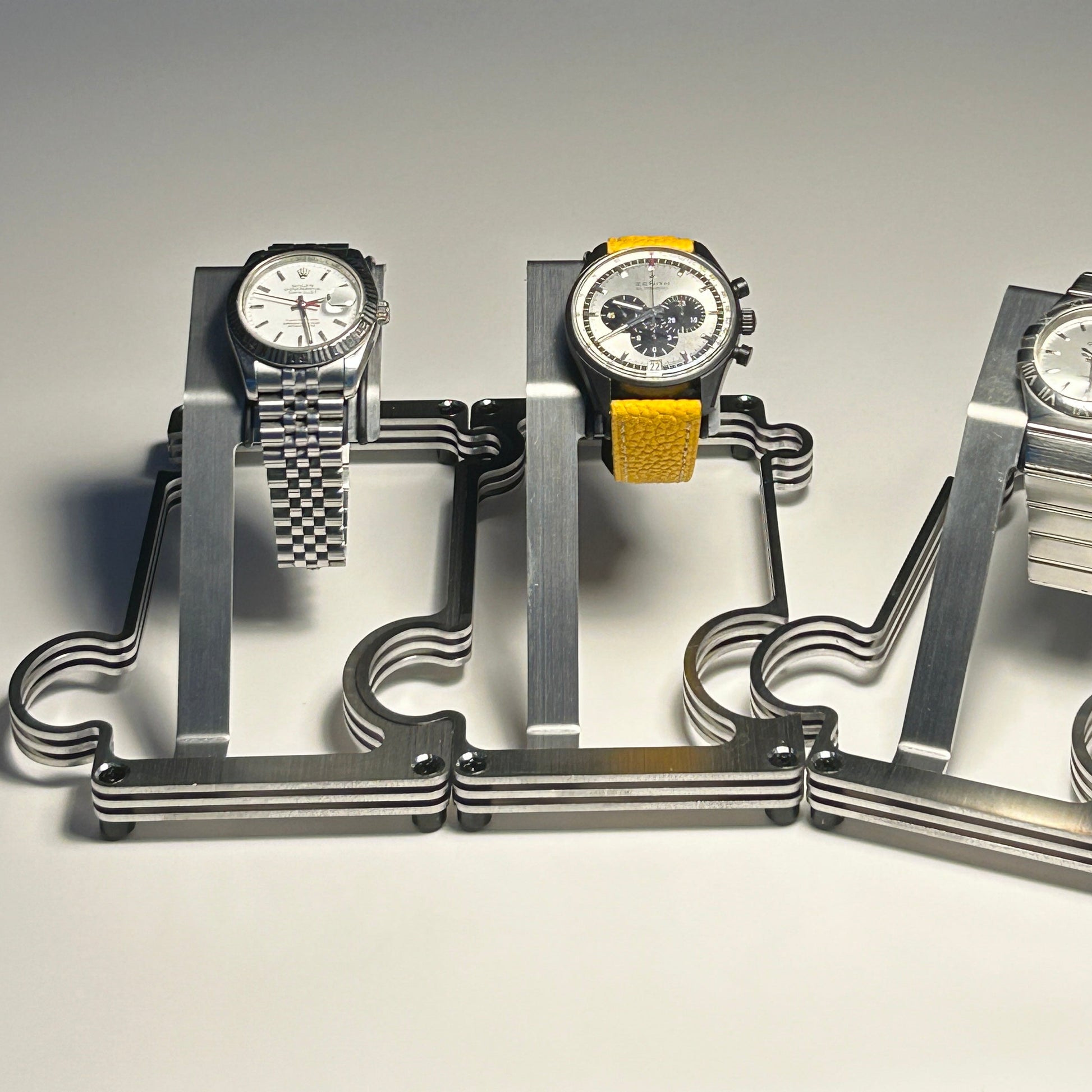 Three watches on a metallic stand against a gray background