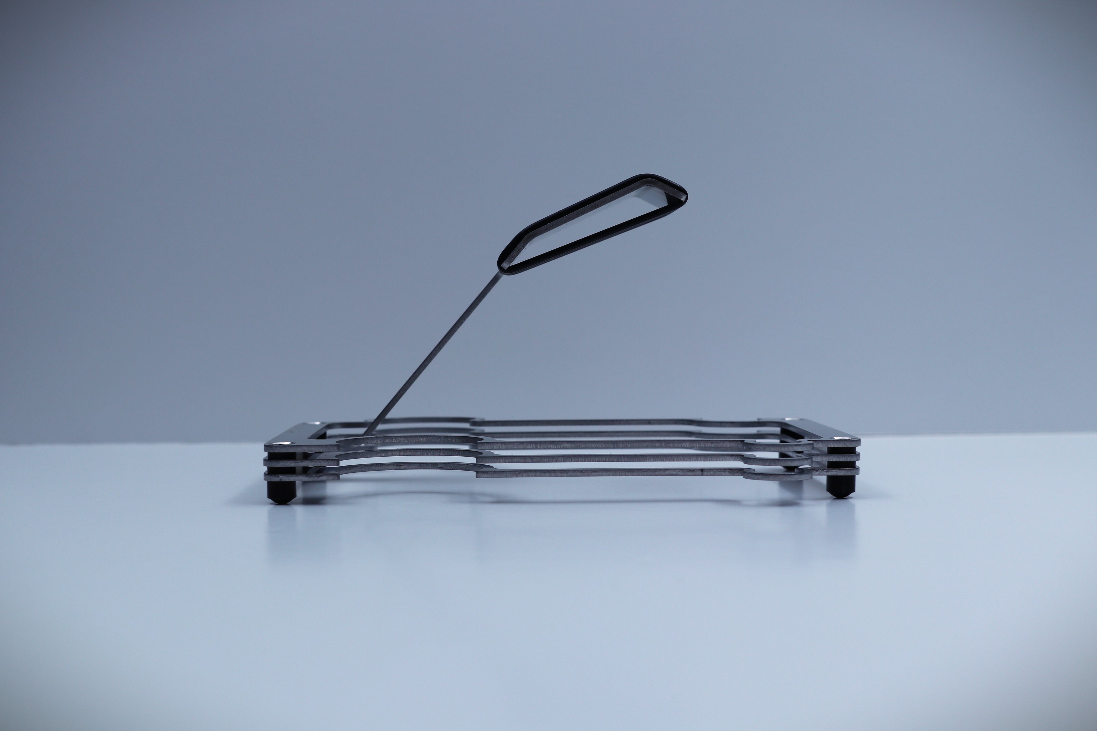 Metal layered to create a watch display holder, shown on a reflective surface with a gradient gray background